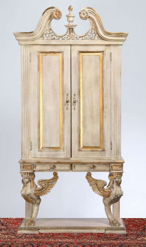 Neoclassical style double door bookcase: Neoclassical style double door raised panel bookcase in an ivory wash with broken arch pediment and central finial all resting on on winged maiden term figures, 84"h x 41"w x 19"d.