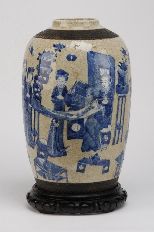 20th c. Japanese earthenware vase: Early 20th century Japanese blue and white earthenware vase decorated with kimono clad figures, scrolls, and tea tables, all raised on a pierce carved wooden base, 18"h x 4.25" diameter top.