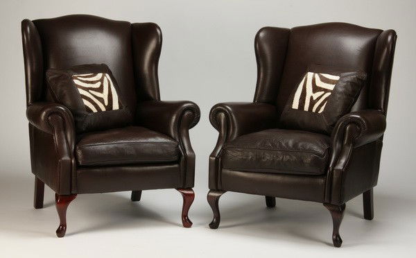 (2) Leather wingback chairs w/ zebra hide: Pair of English wingback chairs upholstered in dark brown leather, each with a throw pillow accented in original zebra skin hide, 43"h x 35"w x 32"d.