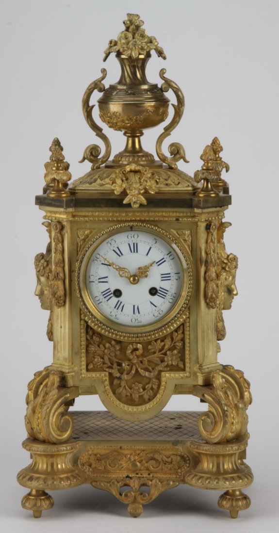 19th c. French dore' bronze clock: Late 19th century Louis XVI style dore' bronze clock, the clock face surmounted by a flower filled urn, the sides with Neoclassical maiden's masks, with applied foliate designs, all raised on scrollin