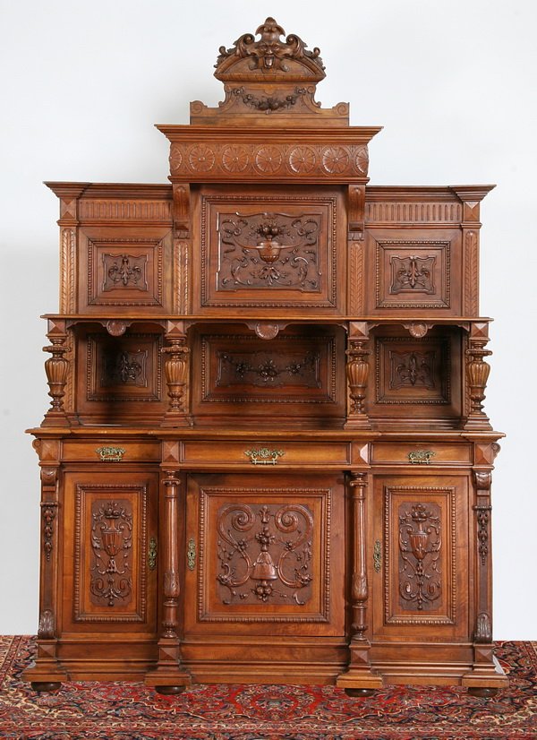 19th c. French walnut buffet: Late 19th century French carved walnut buffet, the crest with Northwind mask, the upper cabinet with foliate carved panels and display shelf raised on baluster form supports, over a three drawer, thre