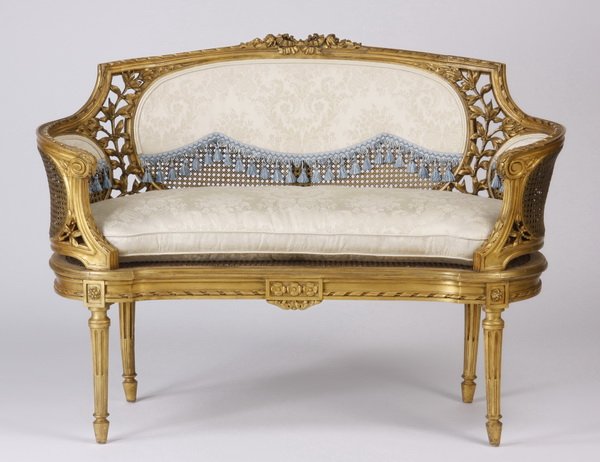 Louis XVI style gilt wood and cane settee: Early 20th century French Louis XVI style carved gilt wood settee with inset woven cane panels joined by pierce carved leaves, the low back and curved sides upholstered in cream silk brocade with blue