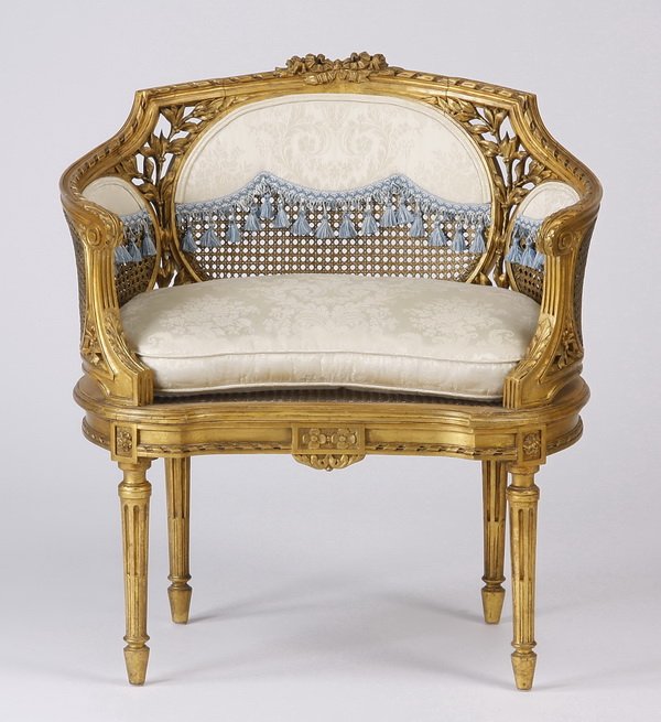Louis XVI style gilt wood and cane bergere: Early 20th century French Louis XVI style carved gilt wood bergere with inset woven cane panels joined by pierce carved leaves, the low back and curved sides upholstered in cream silk brocade with blu