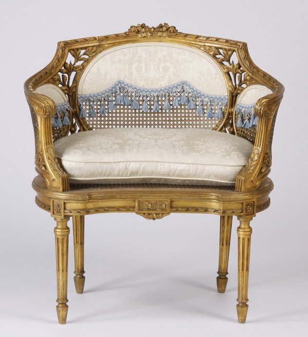 Louis XVI style gilt wood and cane bergere: Early 20th century French Louis XVI style carved gilt wood bergere with inset woven cane panels joined by pierce carved leaves, the low back and curved sides upholstered in cream silk brocade with blu