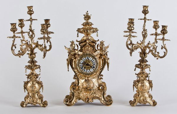 (3) Pc. 19th c. French bronze clock set: 19th century French Louis XV style Rococo Revival dore' bronze clock and garniture set, the clock with a flower filled basket at the crest, and angel term figures amongst shells, swirling acanthus lea