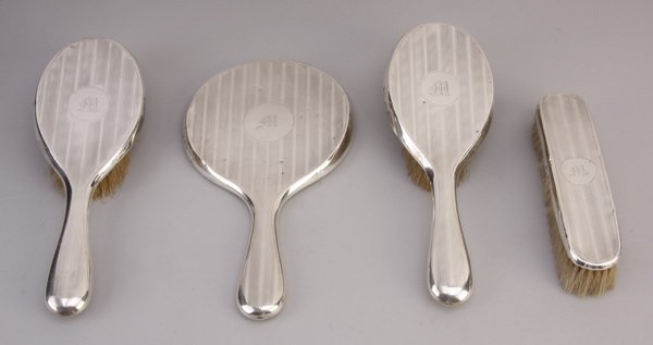 Early 20th c. British sterling vanity set: Early 20th century British sterling silver vanity set, the back of each piece monogrammed with an M, includes (1) handheld beveled glass mirror, (2) hairbrushes, and (1) clothes brush, maker marked J&