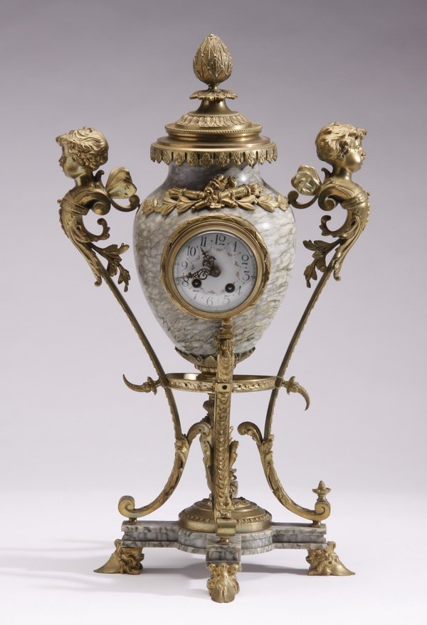 19th c. French gilt bronze and marble clock: 19th century French gilt bronze mounted marble clock in the form of a lidded urn with putti term figure handles, the quadruped marble base raised on animal hoof feet, 21"h.