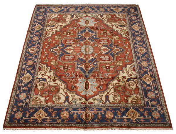 Handknotted Serapi area rug: Serapi rug of handknotted wool with a central rust colored diamond shaped field interspersed with blue and navy, all against an ivory ground, framed by a band of blue, 122"l x 97"w (10' x 8'1").