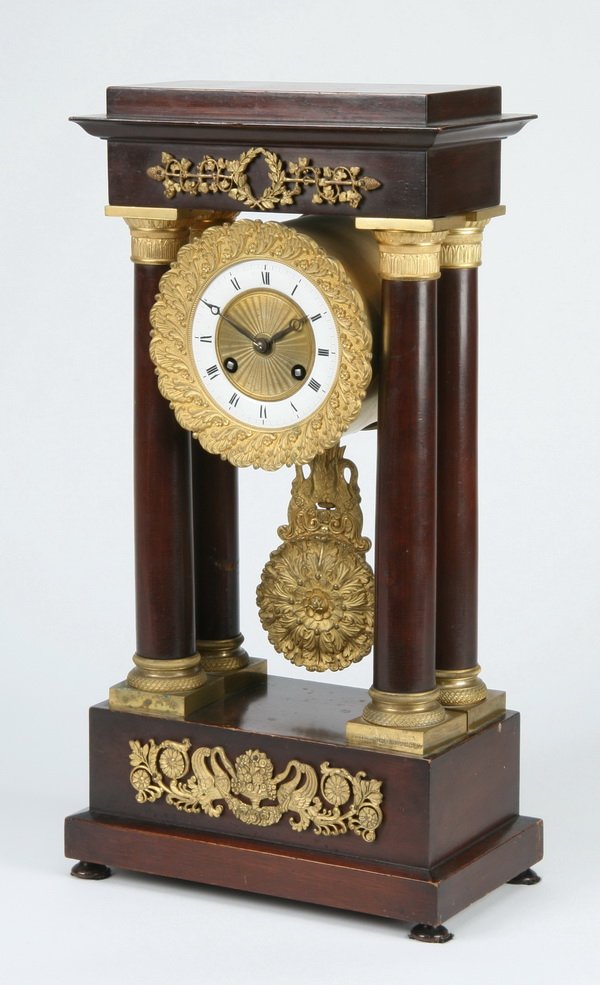 Early 20th c. Empire style portico clock: Early 20th century Empire style mahogany veneered portico mantel clock with gilt bronze mounts, the corniced top over a central porcelain dial with bronze acanthus leaf bezel and pendulum flanked by f