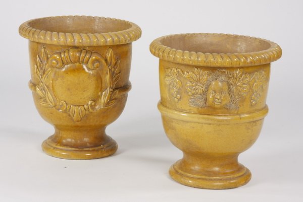 (2) French glazed earthenware jardinieres: Pair of French yellow glazed earthenware jardinieres, each with a gadrooned rim, (1) with a large central foliate decoration and (1) with a janus-form female bust on either side, each 22.5"h x 20" dia