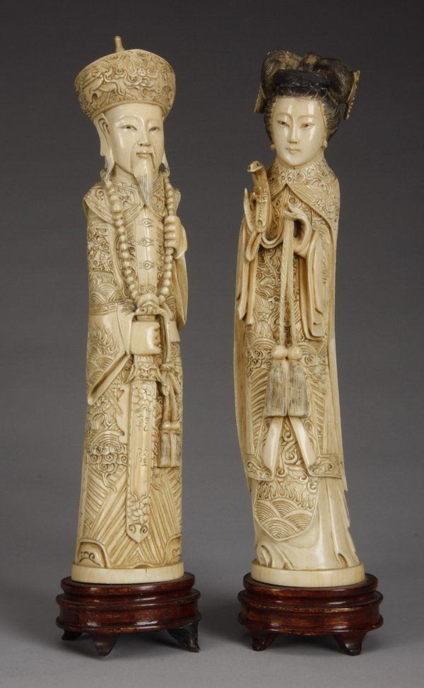 (2) Chinese late Qing Dynasty ivory figures: Pair of Chinese late Qing Dynasty carved ivory figures depicting an emperor and empress in intricately carved robes, the male with Buddhist prayer beads and a sword, the female holding a snake, 12"h x