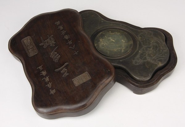 Chinese fan-shaped duan inkstone: Chinese fan-shaped duan inkstone encased in a conforming box, the shaped stone with a central circular water trough and incised decoration of lotus emerging from still water, the lid inscribed, 9"h x 