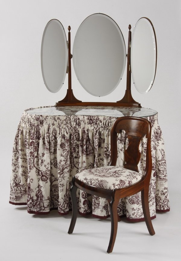 Mid 20th c. mahogany vanity and chair: Early 20th century English carved mahogany skirted vanity and corresponding chair, the vanity with three oval beveled glass mirrors surmounting a kidney shaped body with a custom fabricated protective