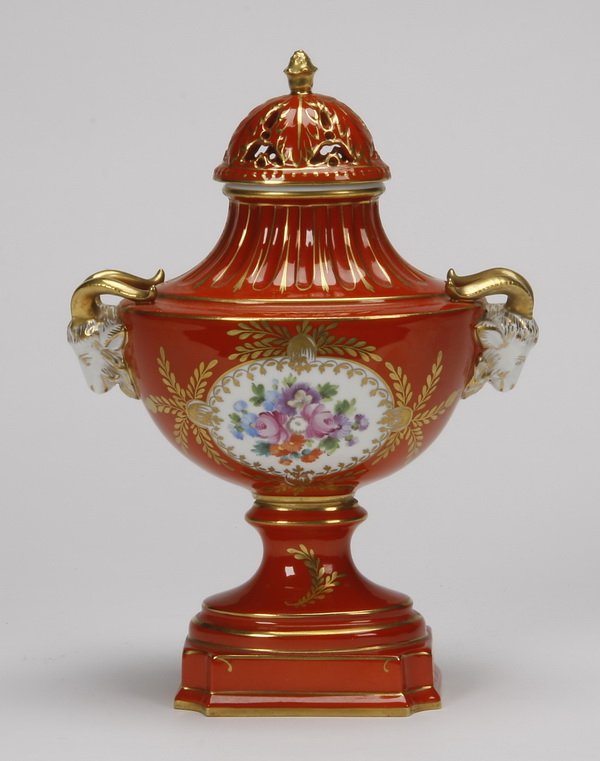 Dresden porcelain urn: Early 20th century German hand painted porcelain lidded urn, the floriate filled cartouches on each side with gilt foliate sprays flanked by ram's head handles, all against a deep orange ground, maker