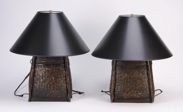 (2) Rattan basket table lamps: Pair of mid to late 20th century hand woven rattan baskets of trapezoidal shape with carrying straps, converted into table lamps, each with an oversized black shade; lamp 24"h x 12"w x 7"d, shade 22"