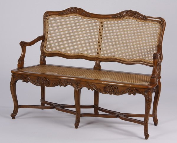 French Provincial style settee: 20th century French Provincial style walnut two seat settee, the floral crest above a woven cane back and seat, joined by curved X-form stretchers and raised on cabriole legs, 40"h x 51"w x 19"d.