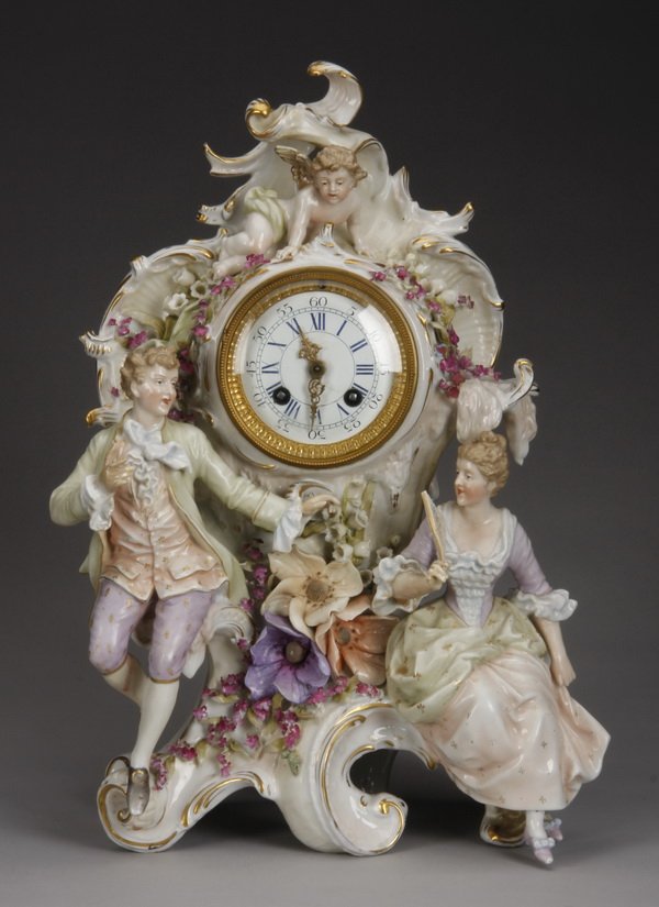 Early 20th c. German porcelain clock, marked: Early 20th century hand decorated German porcelain clock, the asymmetrical rocaille case with a putto at the crest surmounting the dial, a male and female in period dress at the base flanking a centra