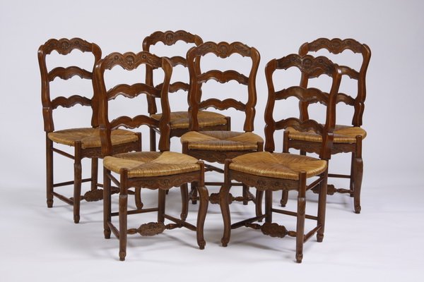 (6) French Provincial style chairs: Set of six 20th century French Provincial style carved walnut side chairs, each with a shell-form crest above a ladder back over a woven rush seat, raised on cabriole legs, joined by an H-shaped stret