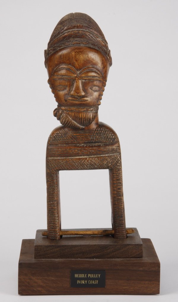 Baule heddle pulley, Ivory Coast: Baule heddle pulley, Ivory Coast, having both functional and aesthetic value, used by a weaver with a narrow-band loom, the carved wood tool embellished with a bearded head finial symbollically guardi