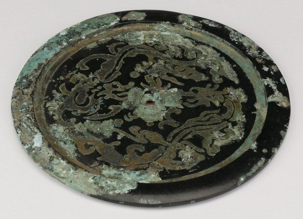 Chinese archaistic Han style bronze mirror: Chinese archaistic Han style bronze mirror, the back with a central knob surrounded by etched decoration of two stylized dragons within a circular border, 8.25" diameter.
