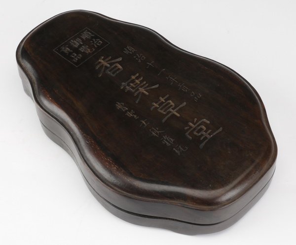19th c. Chinese inkstone: Late 19th or early 20th century Chinese inkstone, the shaped stone with central circular water trough, surmounted by an inscription, encased in a fitted carved zitan box, 10.25"l x 6.75"w x 2"d.