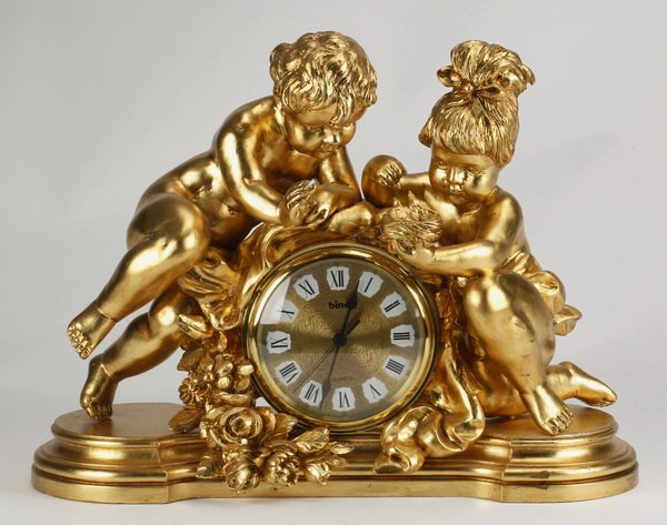 Italian giltwood cherub clock: Italian carved giltwood cherub clock with quartz movement, the two figures examining a birds' nest resting atop the clock, further surrounded by floral garlands, all raised on a shaped base, 17"h x 24