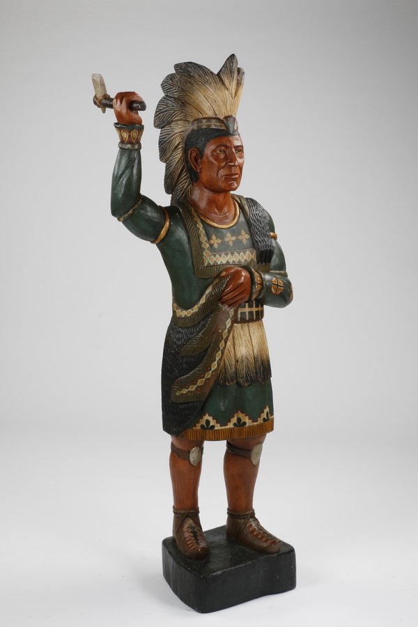 Carved and paint decorated cigar store Indian: Lifesize 20th century cigar store Indian of carved and painted wood, wearing a war bonnet and wielding a tomahawk, upon a square-shaped base, 71"h x 17"w x 16"d.