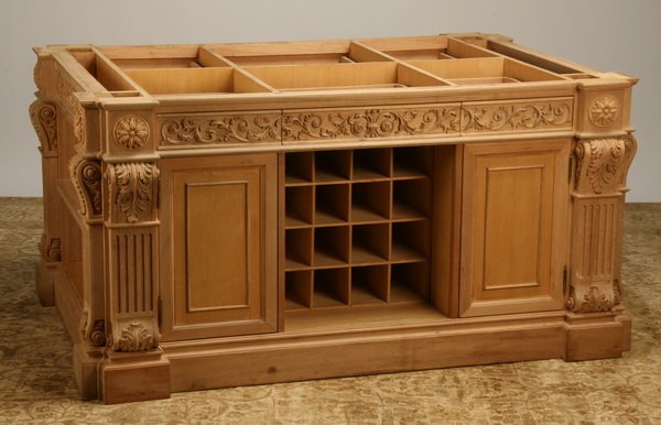 Unfinished carved mahogany cabinet: Unfinished center-of-the-room cabinet of carved mahogany with fluted pilasters and acanthus carved foliage, featuring frieze drawers, open display shelves, concealed storage, and a 16 bottle wine rack