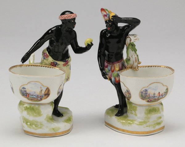 (2) 19th c. KPM figural nut dishes, marked: Pair of 19th century hand painted K.P.M. figural porcelain nut dishes in the form of black-a-moors dressed in colorful skirts, standing beside bowls with paneled scenes of colonial settlers and ships,
