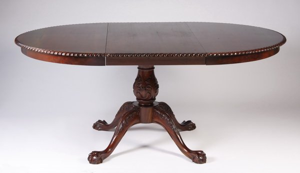 Chippendale style mahogany dining table: 20th century Chippendale style carved mahogany dining table with additional leaf, the round top with gadrooning at the verge, the base with a foliate adorned baluster form standard raised on four legs