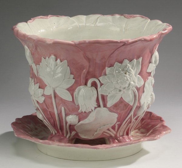 Majolica lotus jardiniere after Minton, 12"h: Majolica jardinire and underplate, of floral form having a shaped rim with a pale blue interior, the exterior decorated with bas relief white lotus flowers on a pink ground, rising on four feet, and r