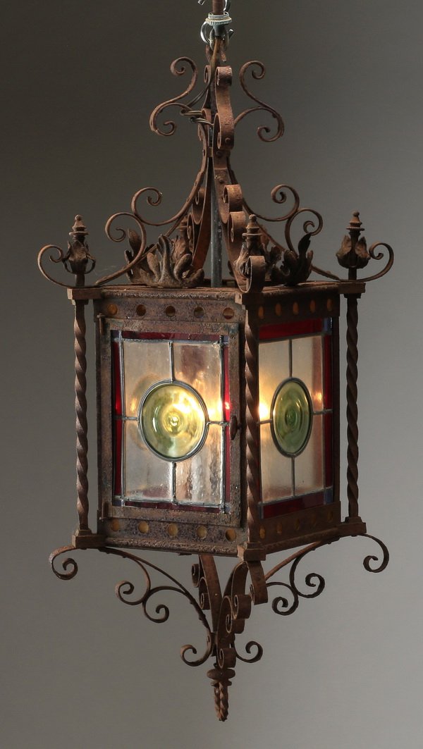 Wrought iron hanging lantern, 30"h: Wrought iron and stained glass hanging lantern, having a scrolled and foliate crest surmounting a rectangular lantern with red, green and clear geometric stained glass sides, and ending in conforming