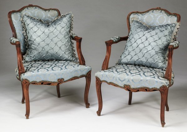 (2) French Louis XV style fauteuils w/ pillows: Pair of French Louis XV style fauteuils, each upholstered in a blue damask fabric with nailhead trim, having shaped backs and open padded carved arms, the whole resting on cabriole legs, 34.5"h x 24"w