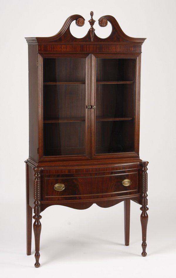 Carved mahogany cabinet on stand, 76"h: Carved mahogany cabinet on stand, the upper cabinet with a broken arched pediment over glass panel double doors opening to shelving, the base with a wide bowed drawer and serpentine apron, flanked by 
