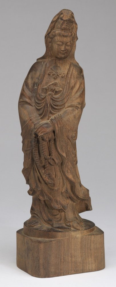 Chinese carved wood figure, Quan Yin, 12"h: Chinese carved wood figure of Quan Yin, the Goddess of Mercy, standing with her hands crossed and holding a long strand of beads, the whole resting on a square plinth, 12"h x 4"w x 2.5"d.