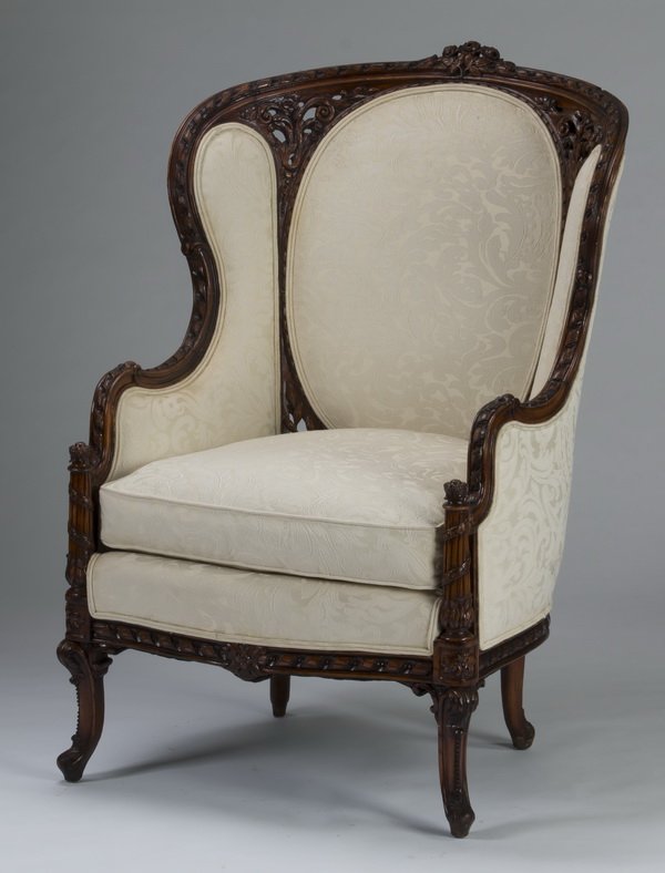 Louis XV style mahogany berger in cream damask: Louis XV style mahogany bergere, having a carved and pierced frame of flowers, braids, and ribbons, and upholstered in a cream damask, the circular back panel and sides over a loose cushion, resting o