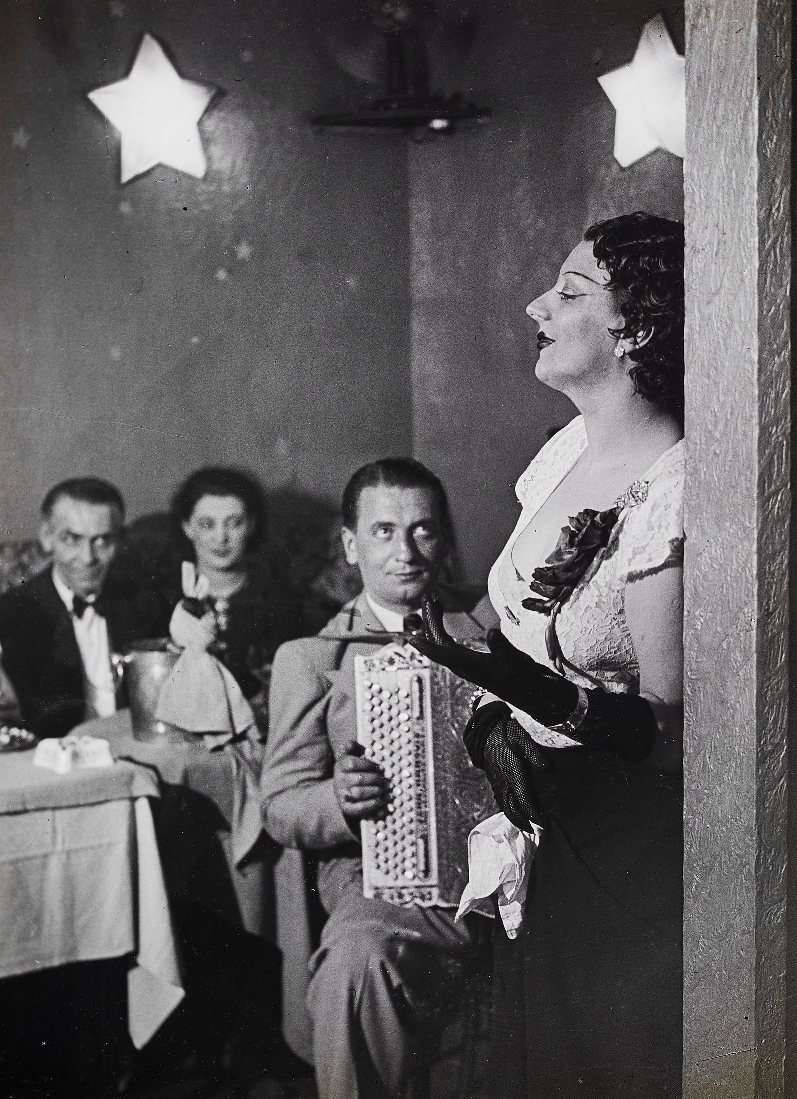 BRASSAI (1899–1984) - Kiki Singing at the Cabaret des Fleurs, Boulevard Montparnasse, 1932*: Gelatin silver print, printed 1972 32,7 x 23,9 cm Signed and numbered by the photographer in ink in the margin lower right, E