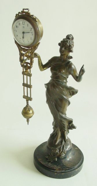 Victorian figural swinger clock: Bronze finish, mounted on wood base. Finish worn. Approx. 15" H. From the NYC estate of Milton & Dorothy Nowack.