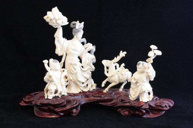 Chinese carved ivory on rosewood base: Depicting "Goddess of Fecundity", bearing tray of peaches, two attendants holding scepters , lotus plant & a Unicorn (creature of good omens, longevity & grandeur). Approx. 7" H x 9" Please read our t