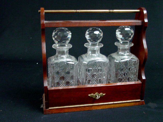 Possibly English 3 bottle tantalus set: Wood, glass & brass. Approx. 14.5" L x 14" H x 5" FD Please read our terms of sale.