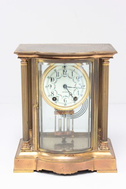 Neo-Classical brass clock by Seth Thomas: With bowed beveled glass panels, fitted with circular enameled dial and mercury weighted pendulum. Approx. 11" H x 9" x 6.25".