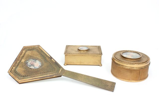 3 piece art deco gilt metal vanity set by Apollo: Consisting of: Round powder box with glass liner, approx. 4.5" Diam. Rectangular box, approx. 5" x 3.5" x 1.5". Hand mirror. All with portraits of "Lady". (3224)
