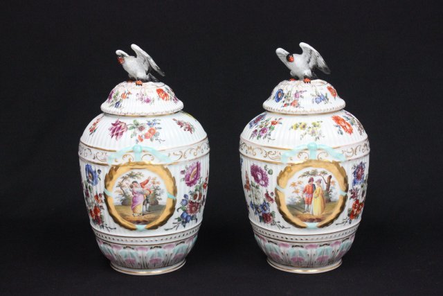 Pair Dresden covered urns with bird finials: Handpainted "Flowers" & "Scene of Blind Mans Bluff & Kissing", chips on beaks. Approx. 13.25" H.