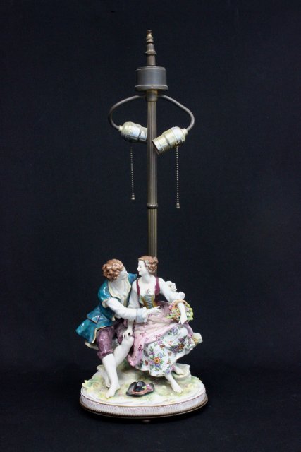 1920's German porcelain grouping mounted as lamp: Depecting "Two lovers sitting on bench". Damage on fingers & toes. Blue maker's mark on back. Figures approx. 12" H. Lamp approx. 29" H