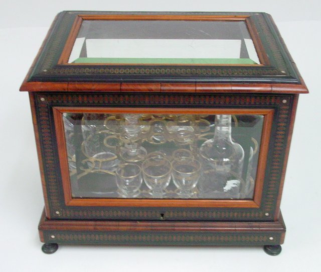 Tantalus Set: Box made of wood with brass inlaid design. Glass sides. Missing 2 bottles & 5 glasses. (3378).