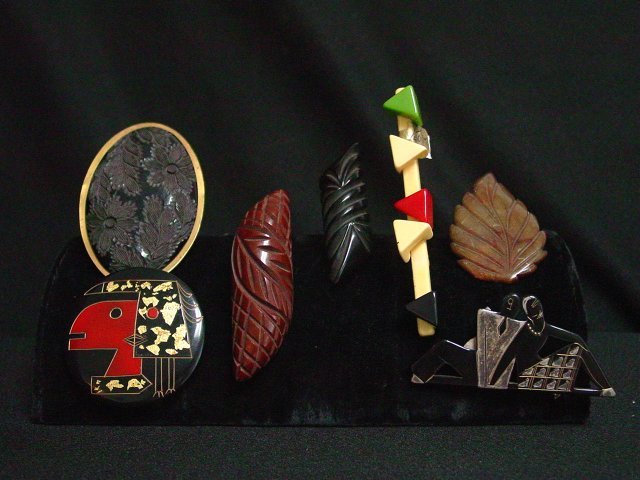 Costume jewelry brooches 7 pieces: Includes 2 carved bakelite brooches in brown and black, 1 Picasso inspired hand painted brooch approx. 2" diam, 1 black floral carved brooch with gold tone metal back, approx. 3 1/8" x 2 1/2". 1 bakel