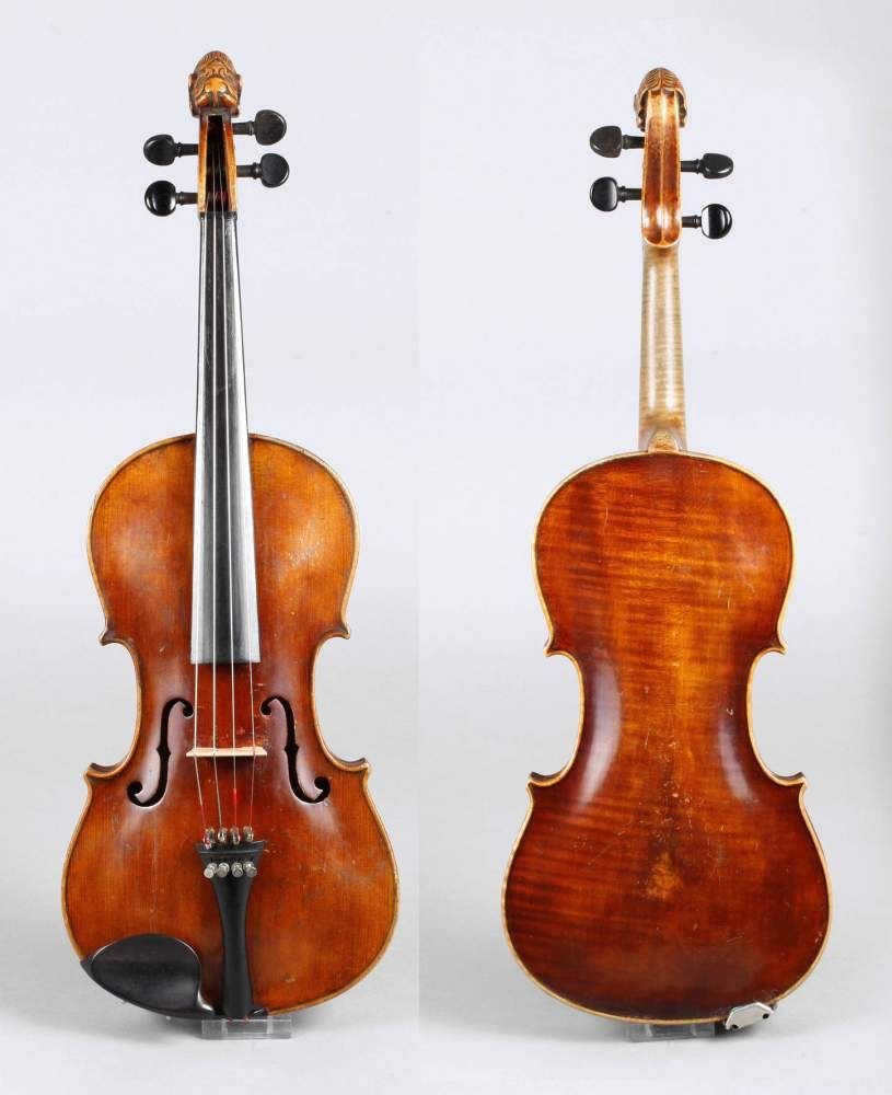 Violine im Kasten: Vogtland, Anfang 20. Jh, ungeteilter, leicht geflammter Boden in mittelbraunem Lack, umlaufende dreiteilige Randeinlage, Wirbelkasten figŸrlich beschnitzt, Decke mit verfestigtem Riss, Zarge rep.bed.
