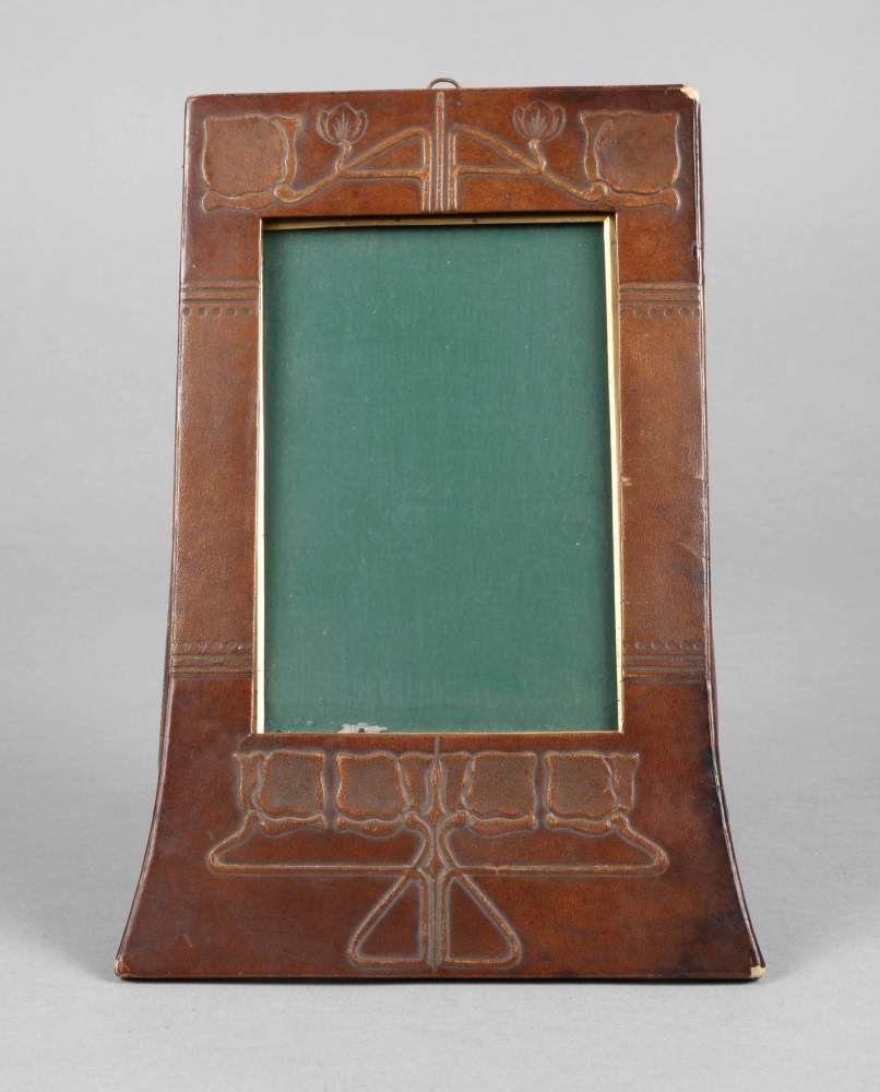 Tischbilderrahmen Jugendstil: um 1900, hochrechteckiges Format, Leiste mit hellbraunem geprgten Glattlederbezug mit Ornamentdekor, orig. Verglasung, rckseitig mit Aufsteller, kleinere Erhaltungsmngel, Mae 24 x 17 cm, Bildausschnit