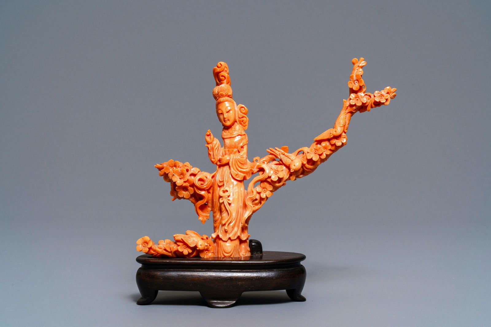 A Chinese carved red coral group of a lady among: A Chinese carved red coral group of a lady among blossoming branches, 19th C. -- H.: 19,5 cm (incl. stand)Weight: 415 gr. (incl. stand)