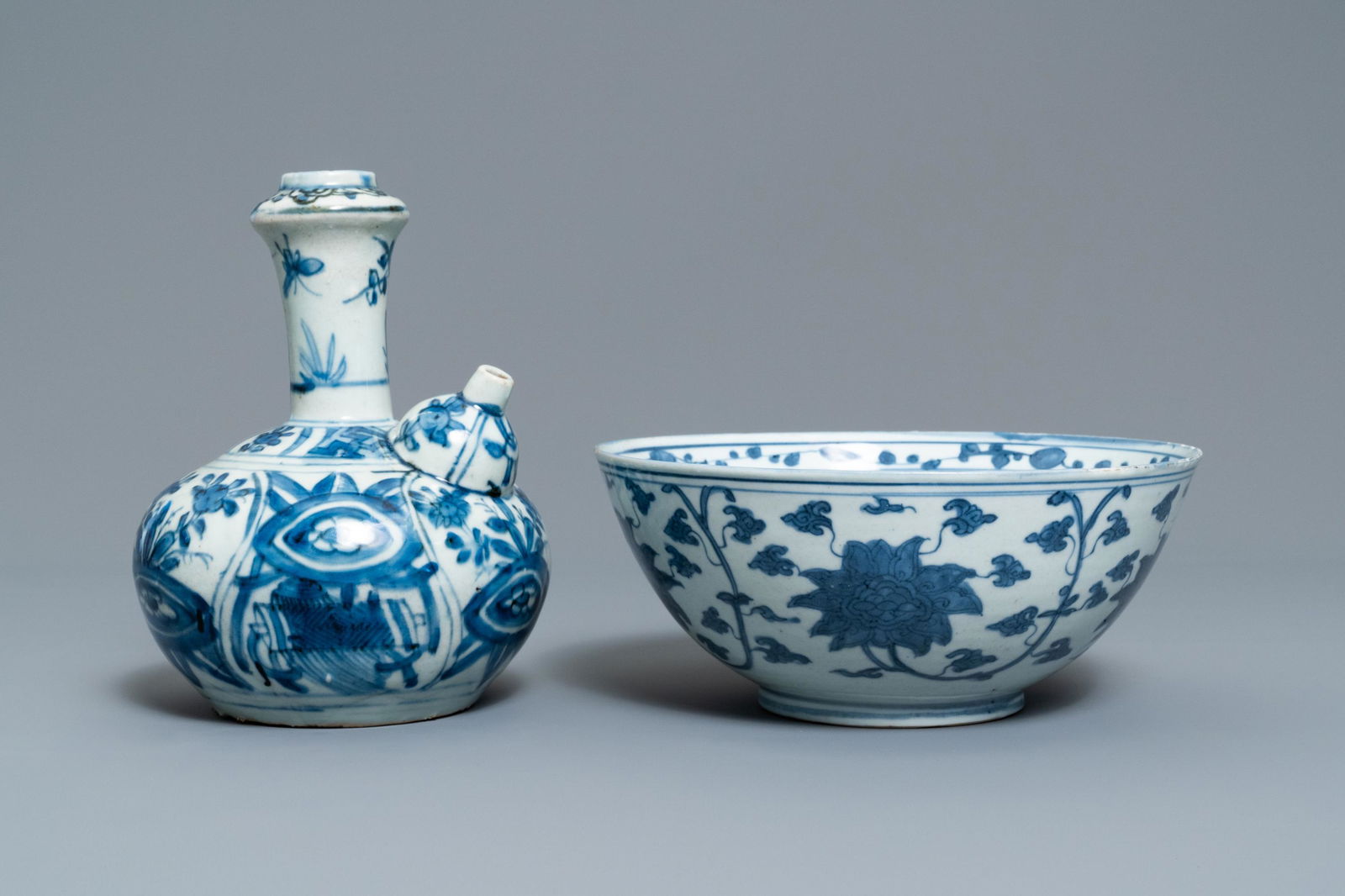 A Chinese blue and white kendi and a 'lotus scroll': A Chinese blue and white kendi and a 'lotus scroll' bowl, Ming Dia.: 20,5 cm - H.: 9,5 cm (the bowl) H.: 19,5 cm - L.: 14,5 cm (the kendi) Condition: (UV-checked) - The bowl with a ca. 10 cm hairlin